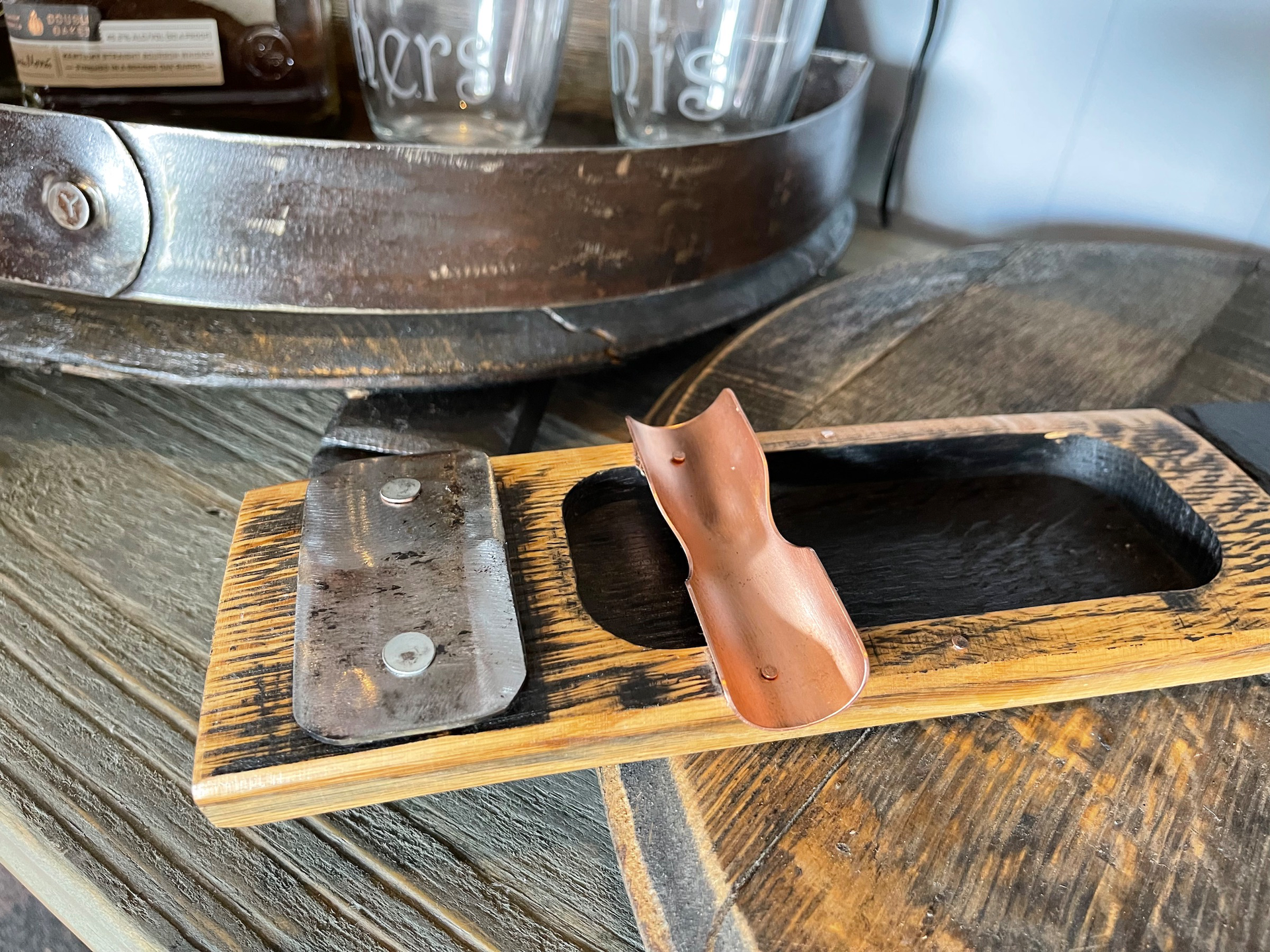 A wooden tray with two glasses on it is on a wooden table.