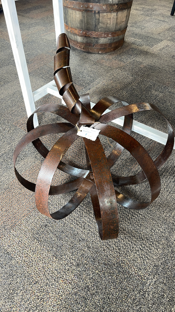 A metal sculpture is sitting on the floor next to a wooden barrel.