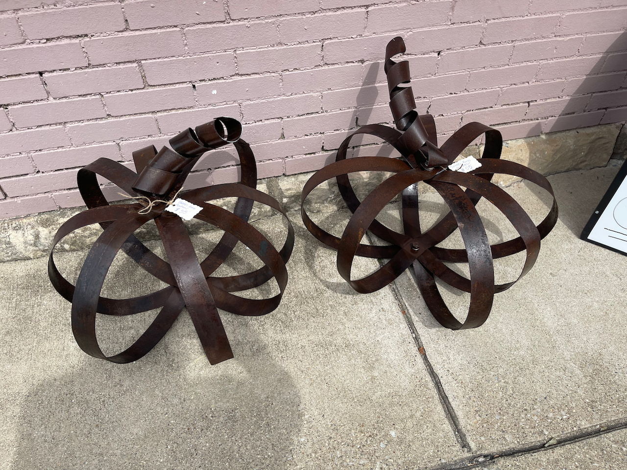Two brown metal sculptures are sitting on a sidewalk in front of a brick wall.