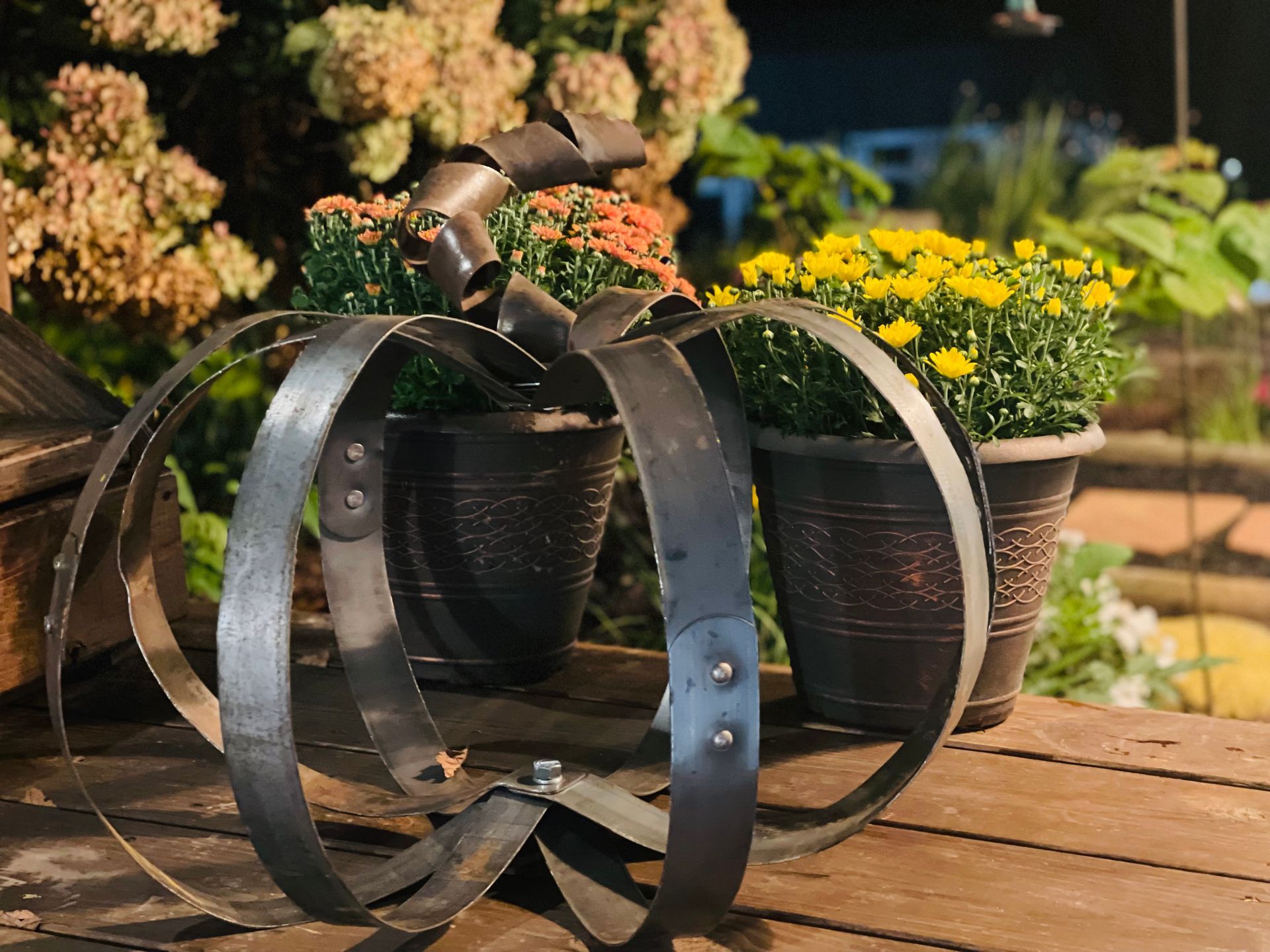 A metal pumpkin is sitting on a wooden table next to potted plants.