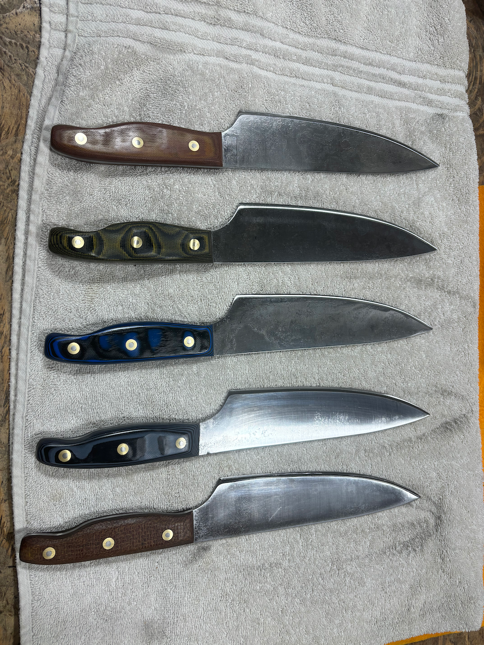 Five knives are lined up on a towel on a table.