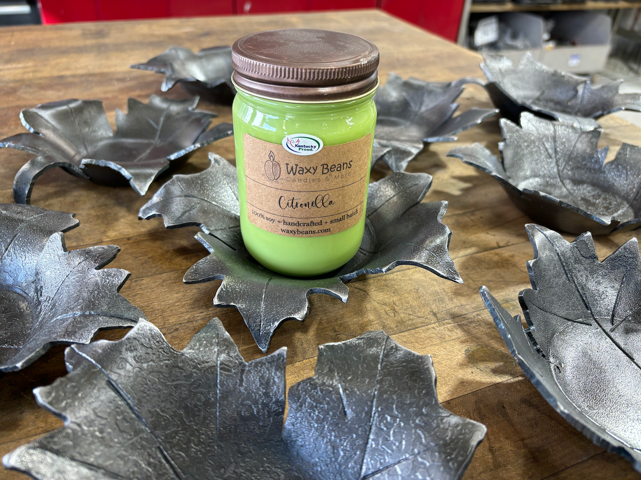 A green candle is sitting on top of a wooden table surrounded by metal leaves.