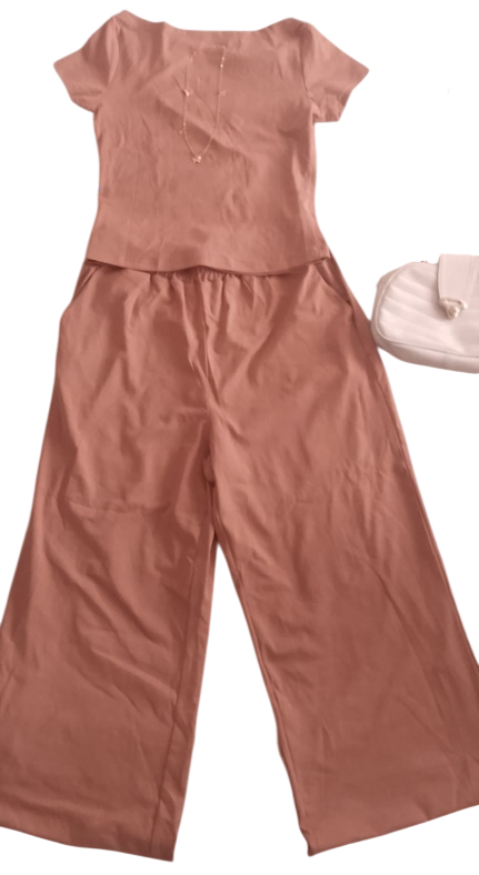 Traje de pantalón color melocotón con camiseta de manga corta y pantalones anchos; al lado hay un bolso de mano blanco.