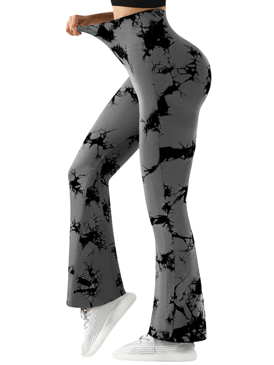 Mujer con leggings acampanados con efecto tie-dye de color gris y negro y zapatillas blancas, de pie sobre un fondo blanco.