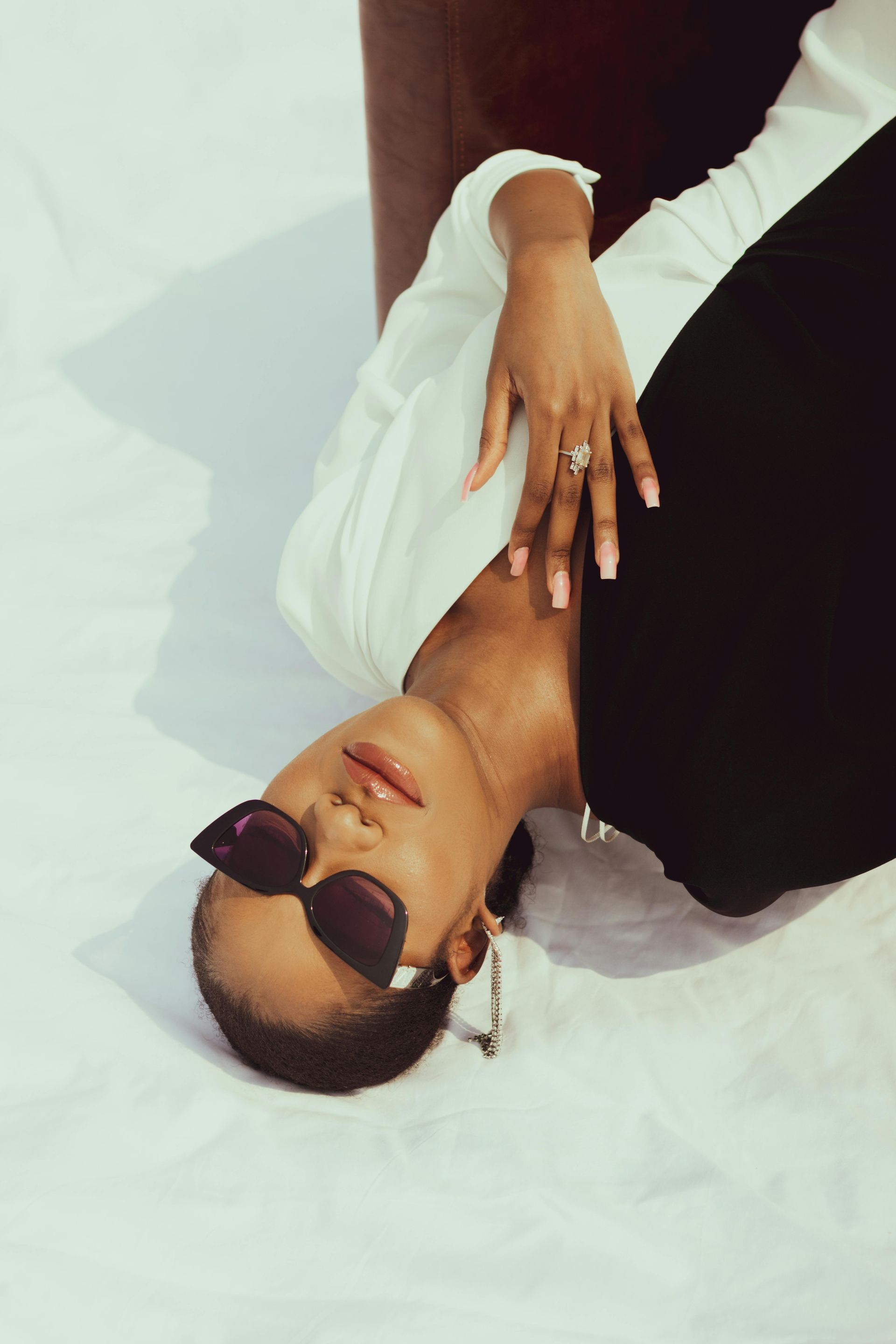 Mujer con gafas de sol, reclinada sobre una superficie blanca con un brazo levantado.