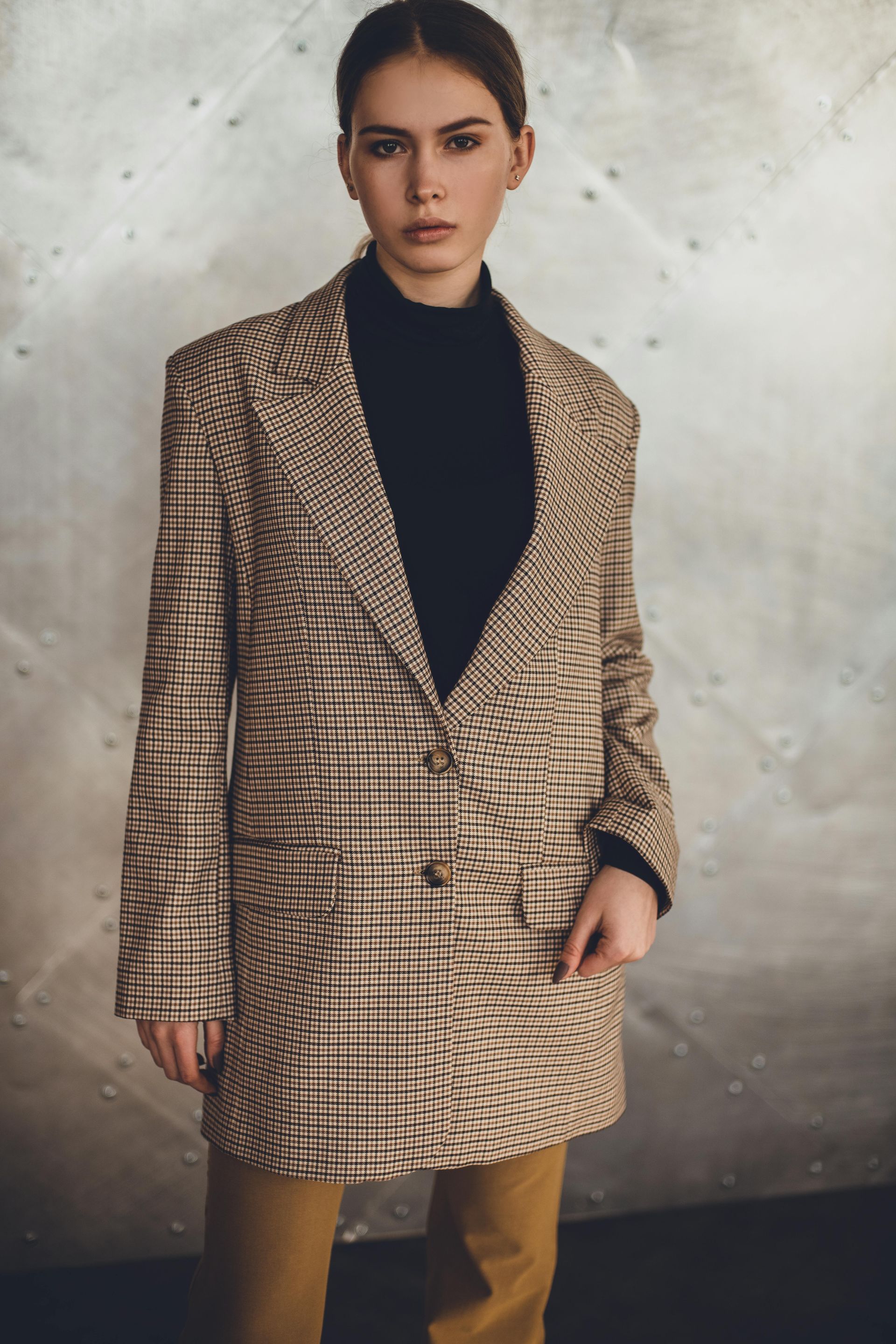 Mujer que viste un blazer a cuadros sobre un jersey de cuello alto negro y pantalones color canela
