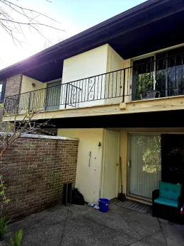 Two-story building with balconies. Brick wall on the left, sliding glass doors on the right, outdoor seating.
