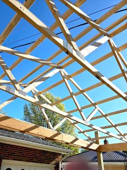 Wooden roof framing against a bright blue sky. Construction on a home's extension is underway.