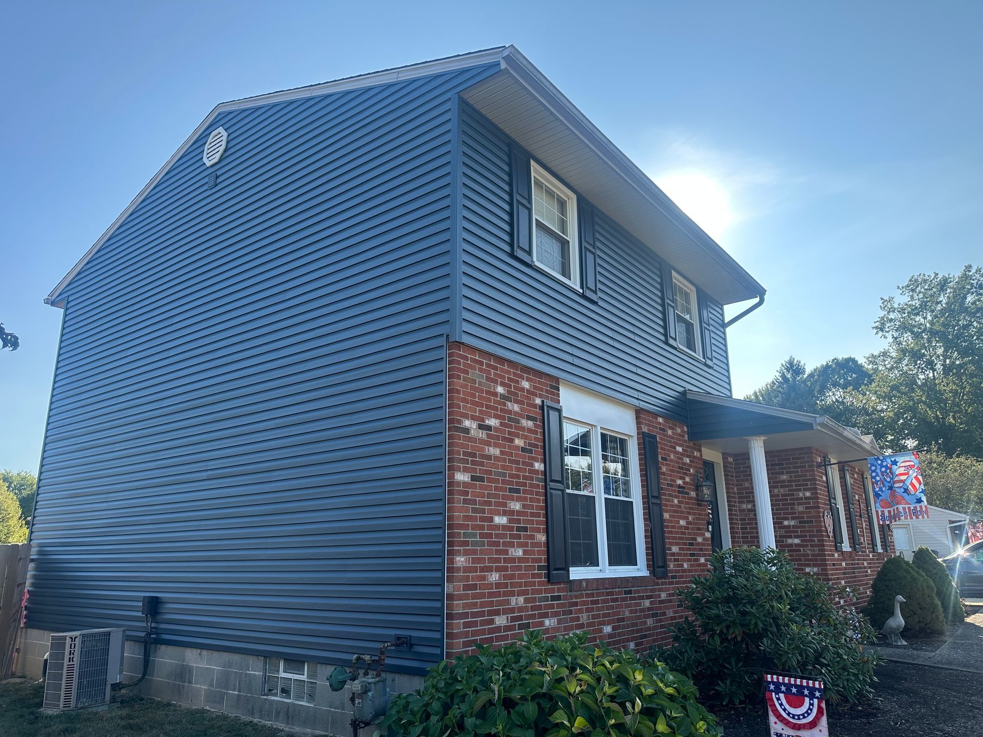 Two-story house with blue siding and brick facade under a sunny sky.