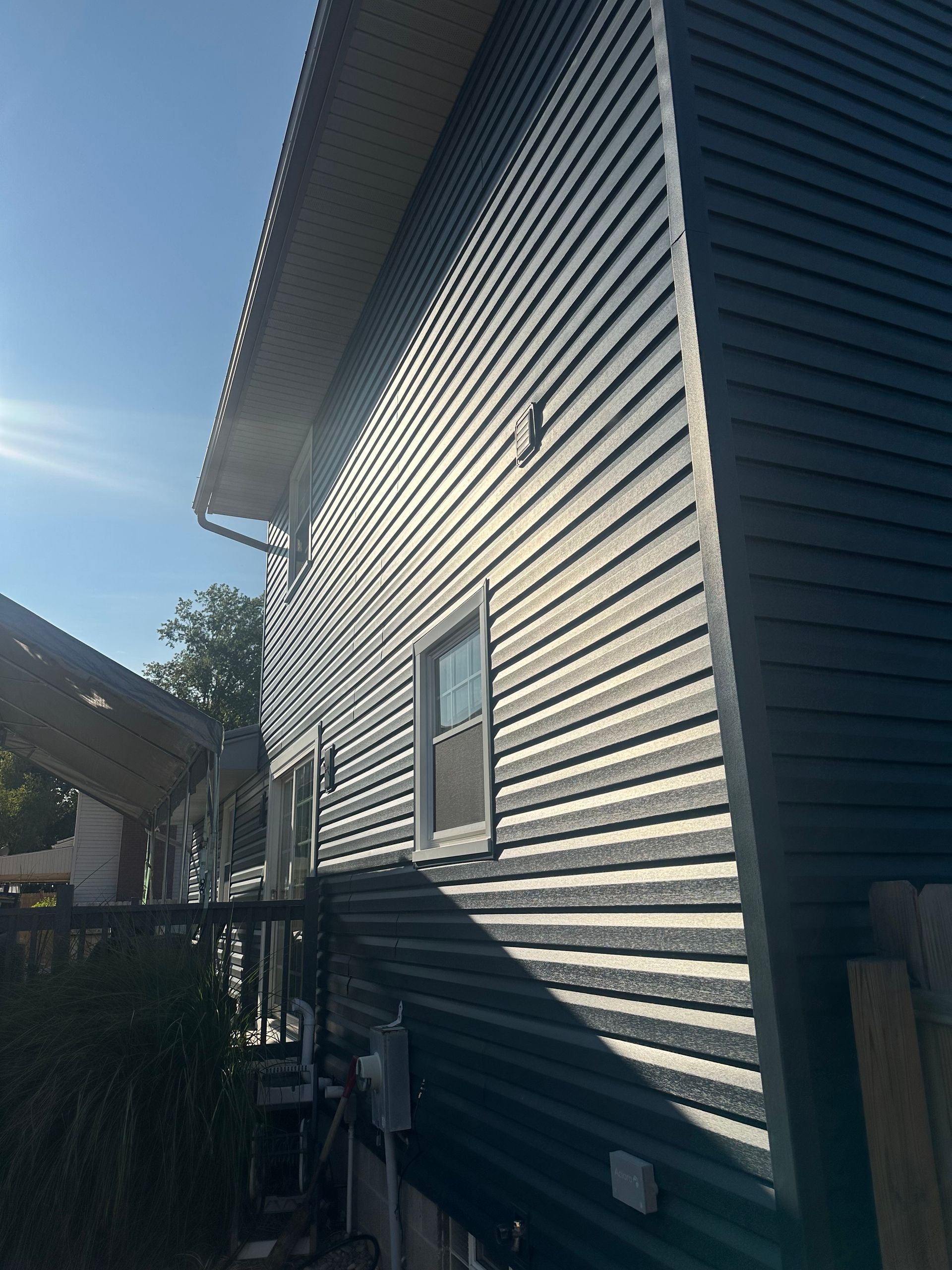Dark blue siding on a two-story house with a window, under a bright blue sky.