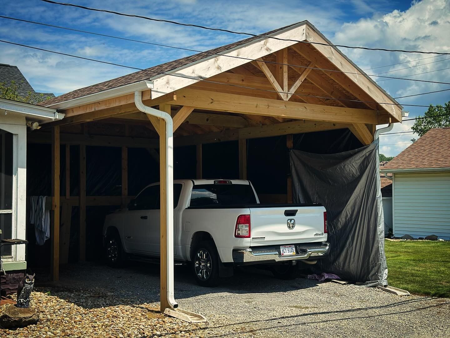 White pickup truck parked under a wooden carport attached to a house with a cloudy sky.