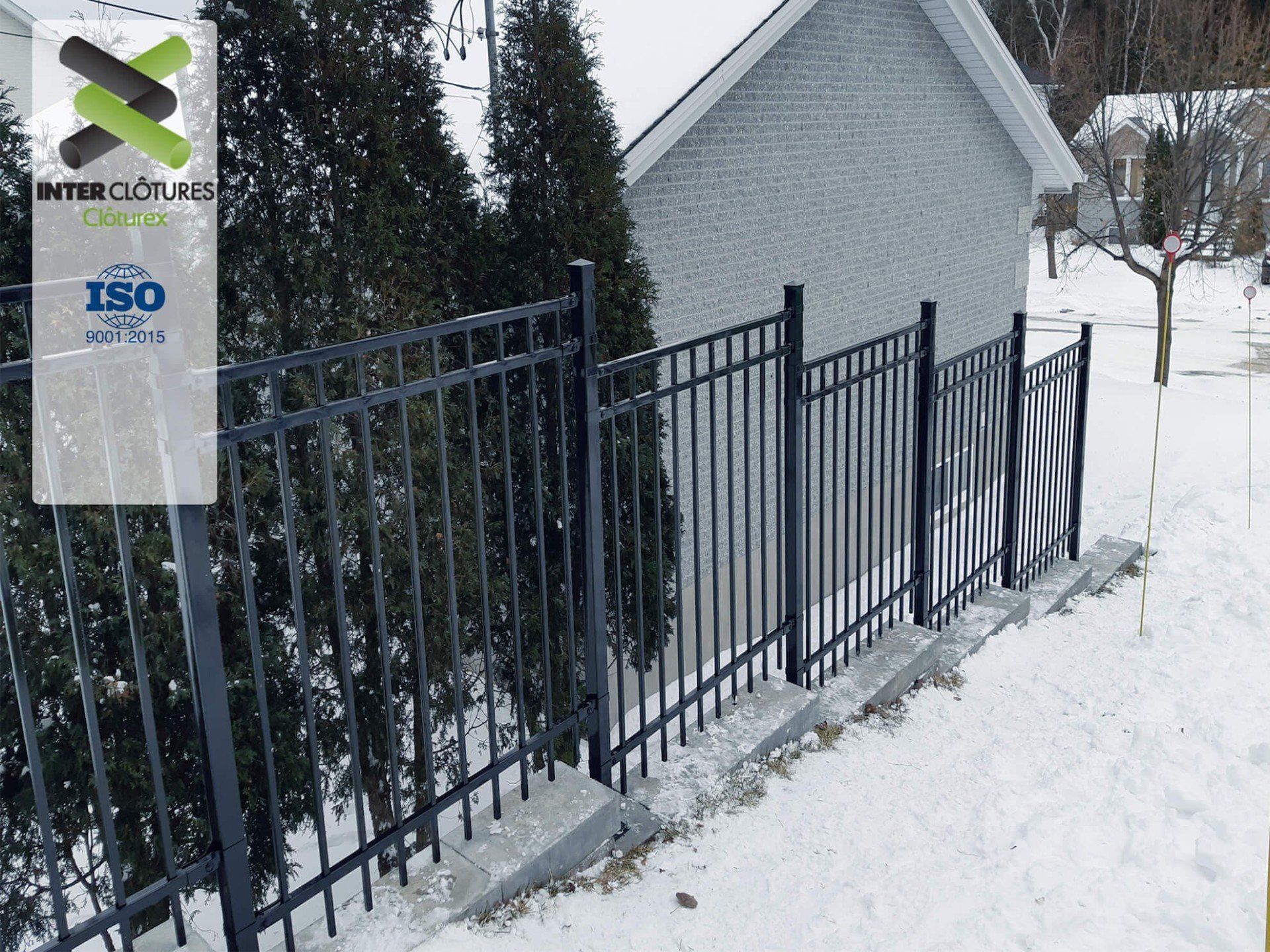 Une clôture en fer forgé est devant une maison sous la neige