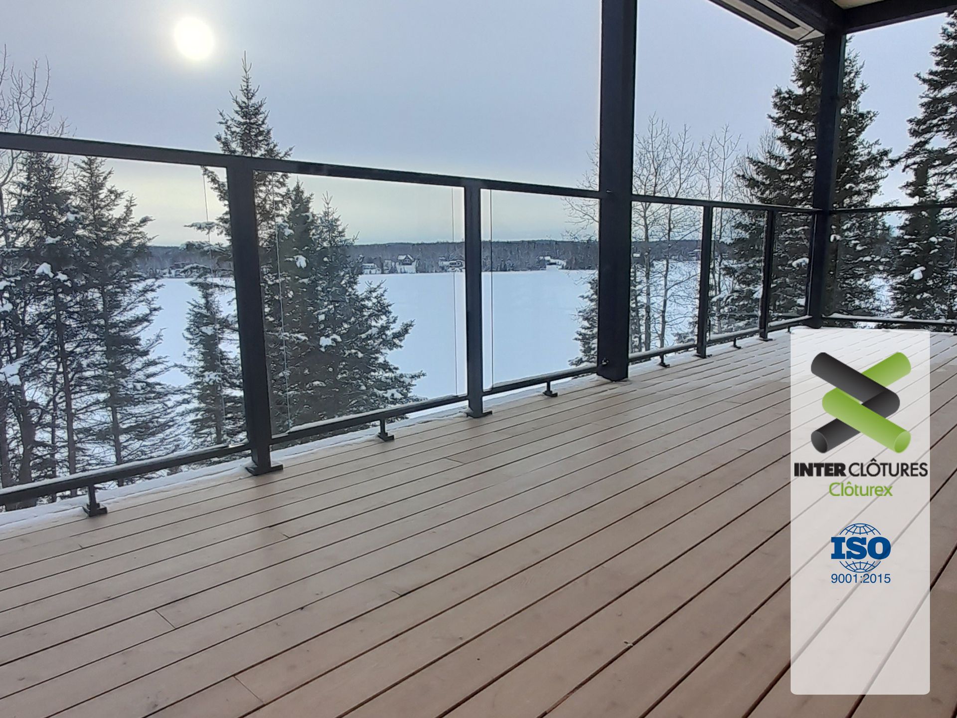 Une terrasse en bois avec une balustrade en verre donnant sur un lac