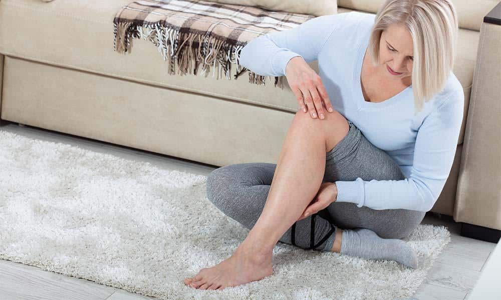 A woman is sitting on the floor holding her leg in pain.