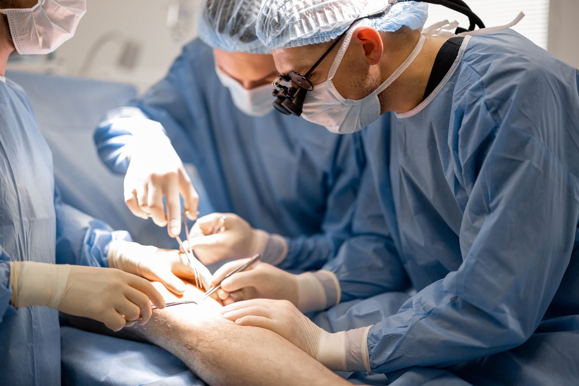 Medical team performs a procedure on a patient’s leg in a brightly lit operating room. Medical team performs a procedure on a patient’s leg in a brightly lit operating room.
