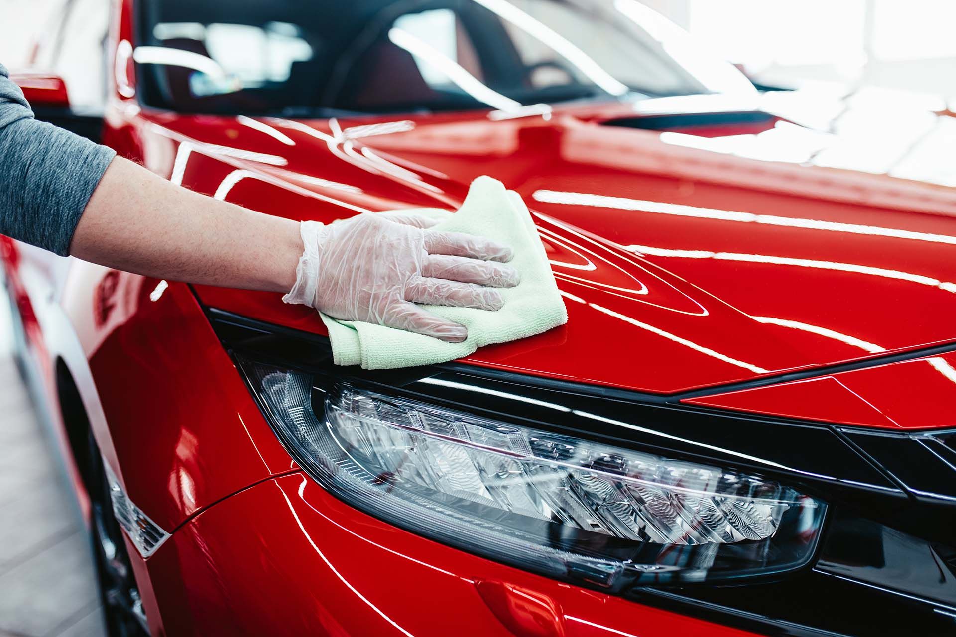 Professionally hand polishing a red vehicle for a showroom finish at a local car wash.