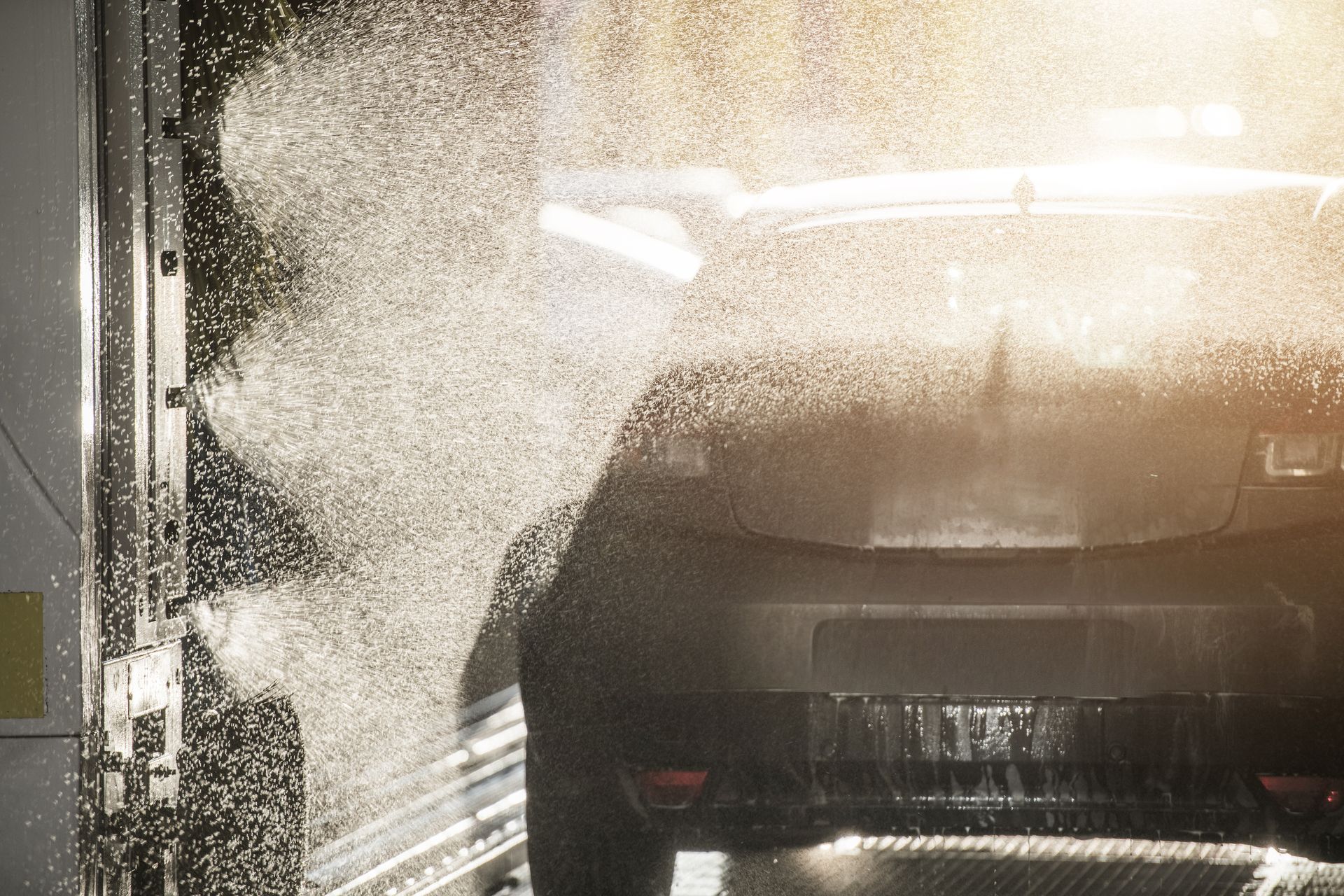 Rear view of a car being rinsed with high-pressure water in an automatic car wash.