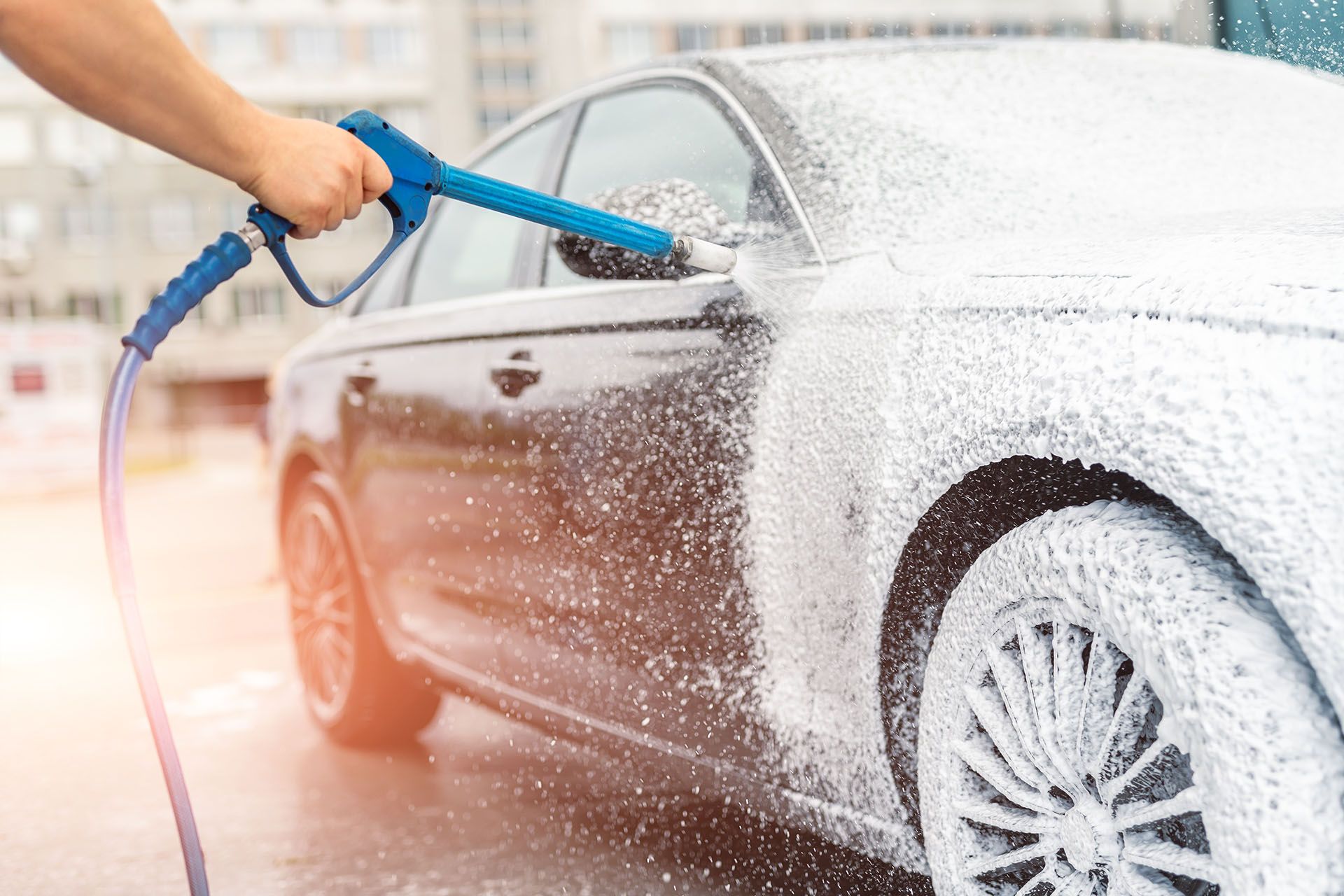 A high-pressure foam cannon spraying a luxury car during a professional car wash service. A high-pressure foam cannon spraying a luxury car during a professional car wash service.