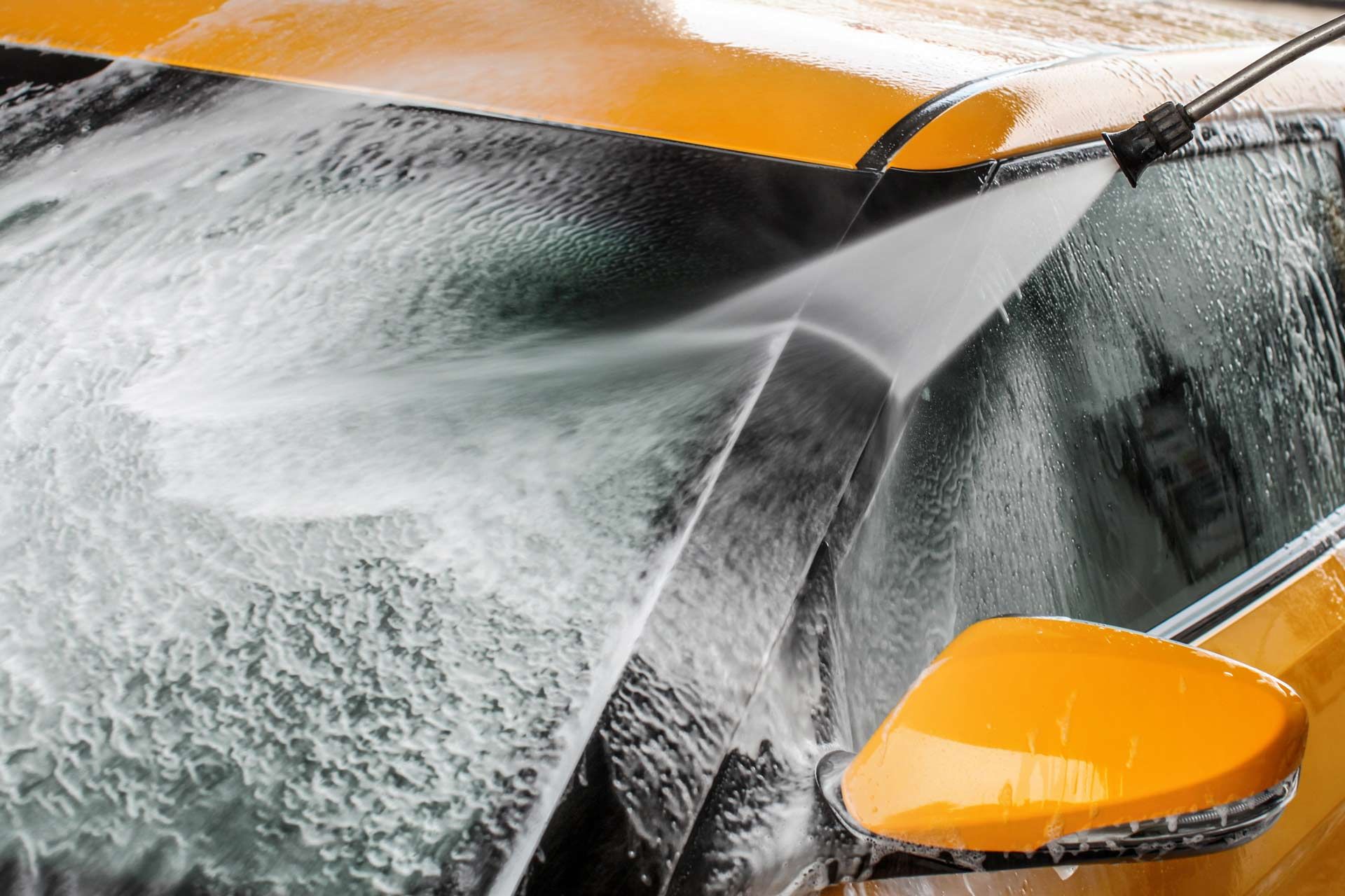 Detail of a car windshield and mirror being cleaned with water jet spray at a car wash service