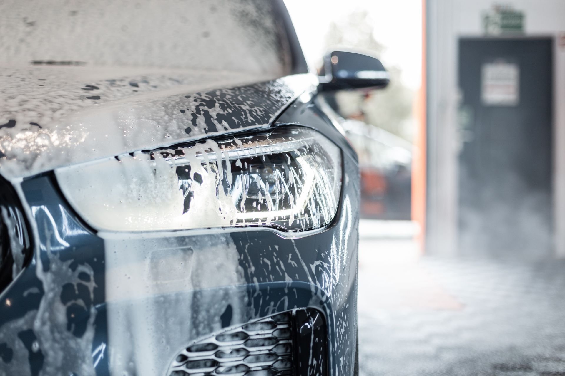 Car covered in foam with shining headlights inside the garage car wash. 