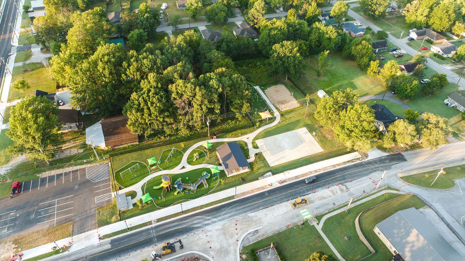 Aerial view of a park with playground, trees, houses, and road.