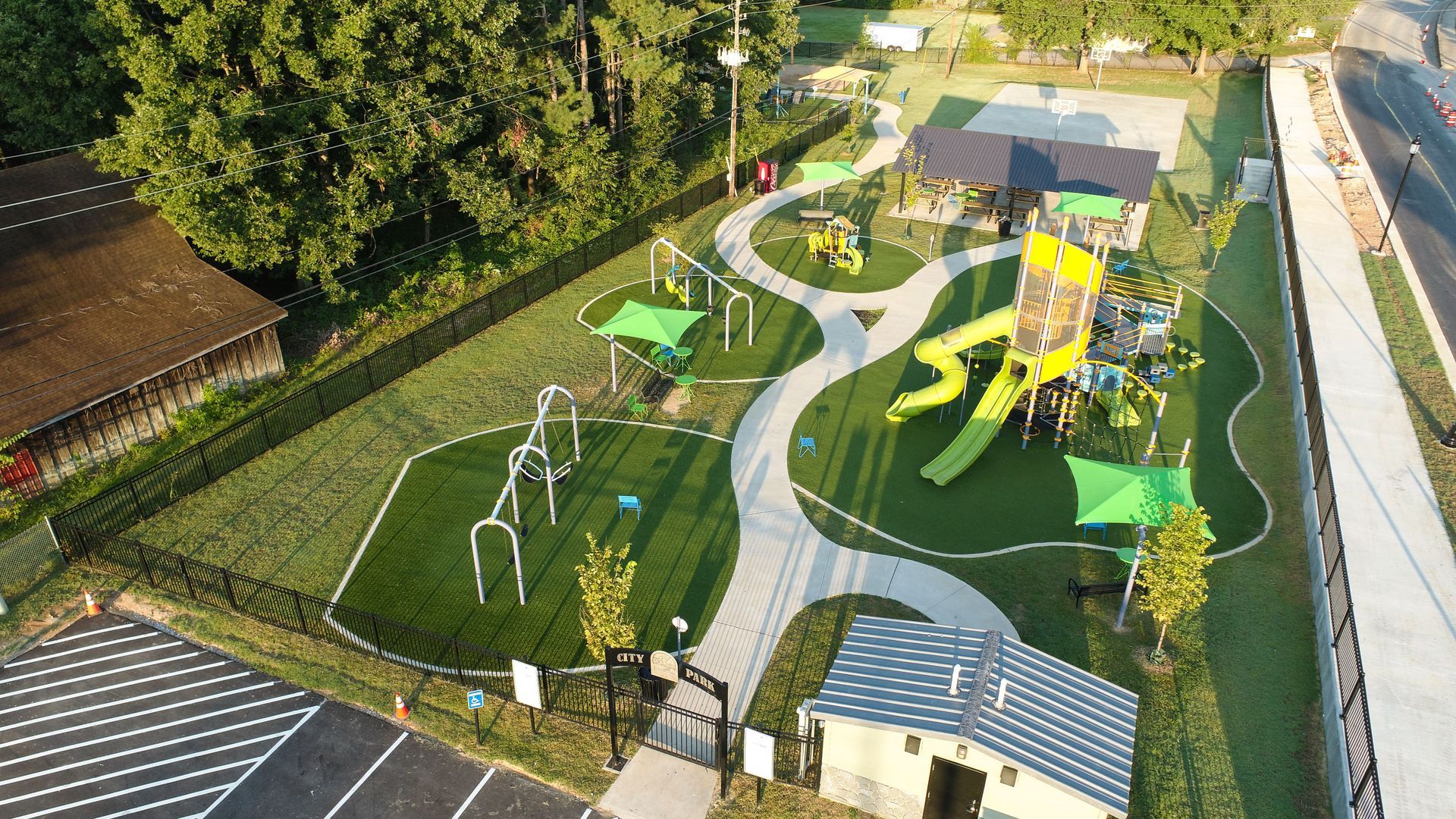 Aerial view of a playground with winding pathways, climbing structures, slides, and shaded areas, surrounded by green space.