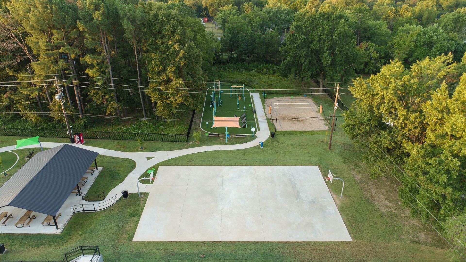 Park with playground, pavilion, and concrete area surrounded by grass and trees.