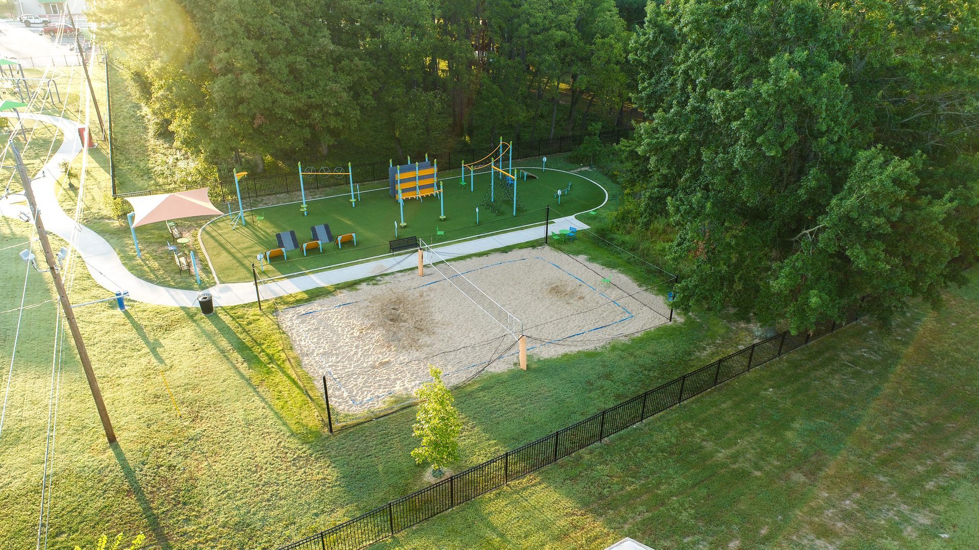 Aerial view of an outdoor sports complex with a sand volleyball court, workout area, and a shaded seating area.