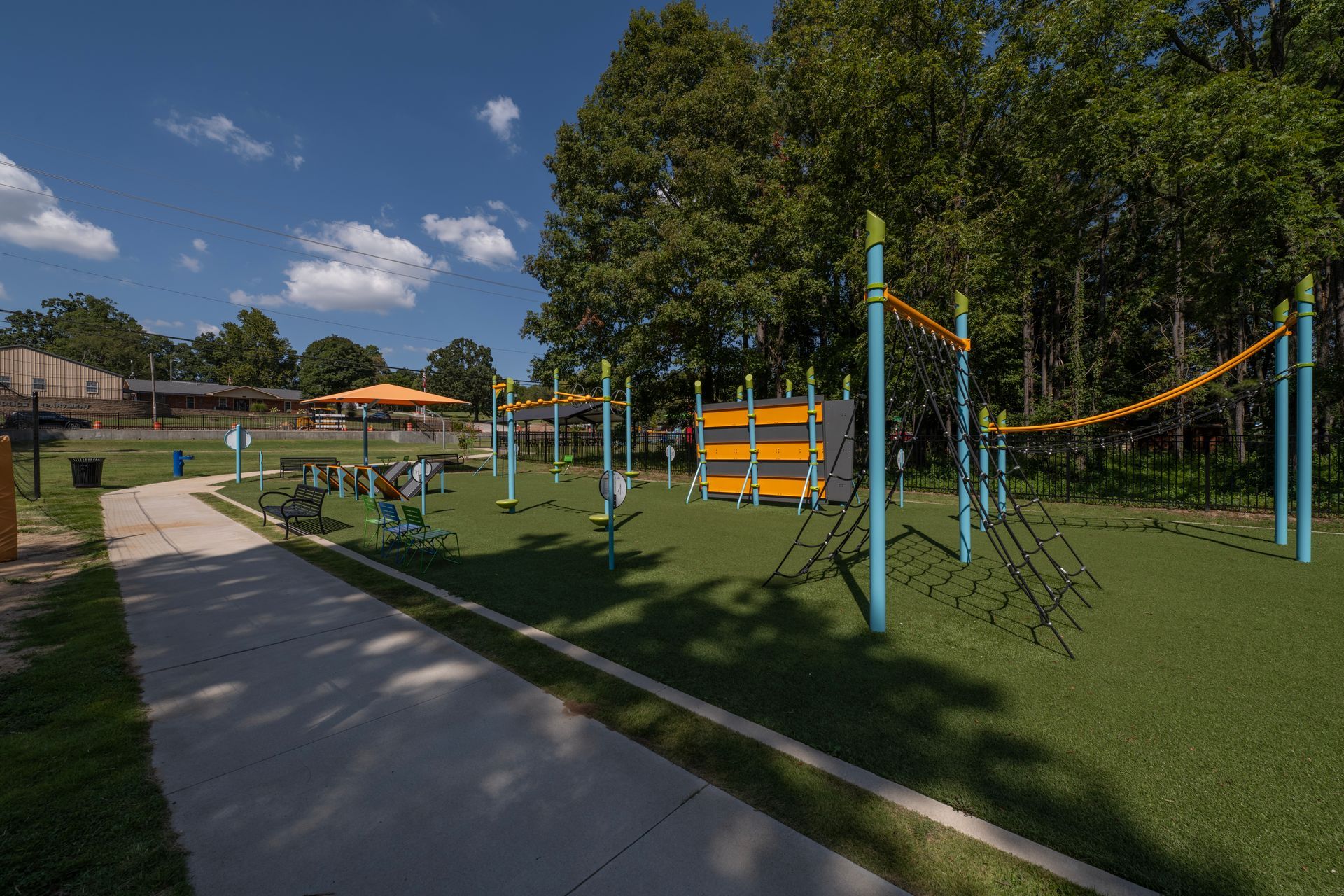 Playground with blue and yellow equipment, green turf, and paved walkway under a blue sky.
