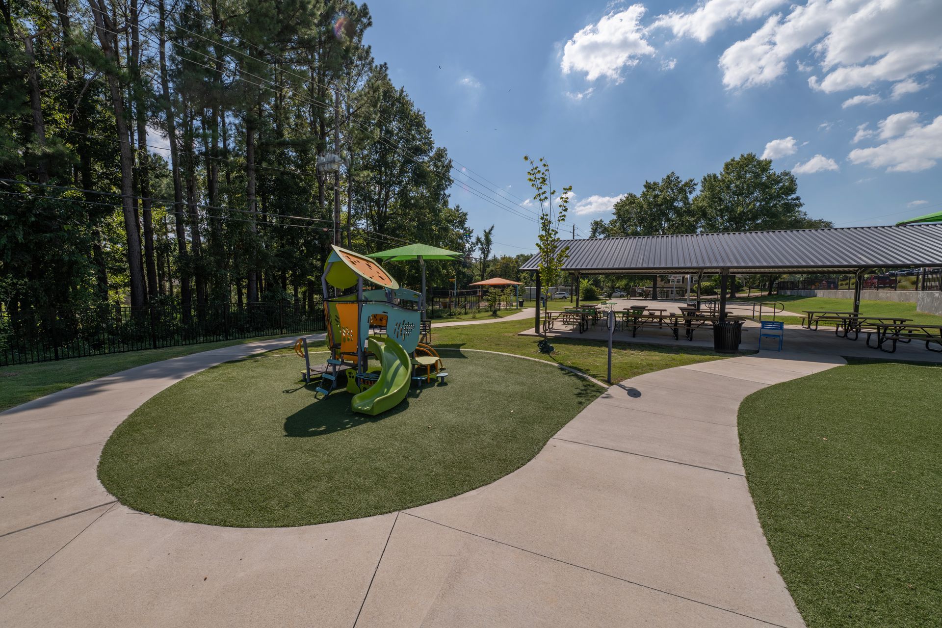 Park playground with green slide and shelter with picnic tables under a blue sky.
