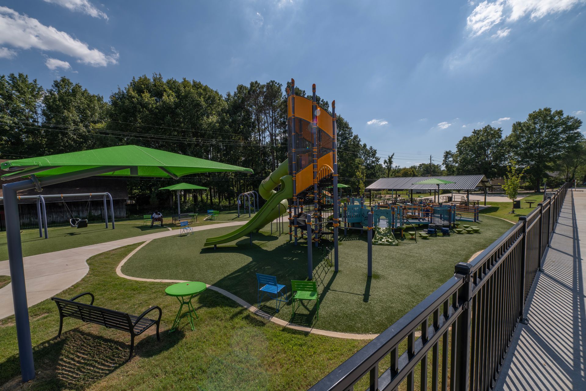 Playground with green shade structures, a tall slide, and accessible features, on a sunny day.