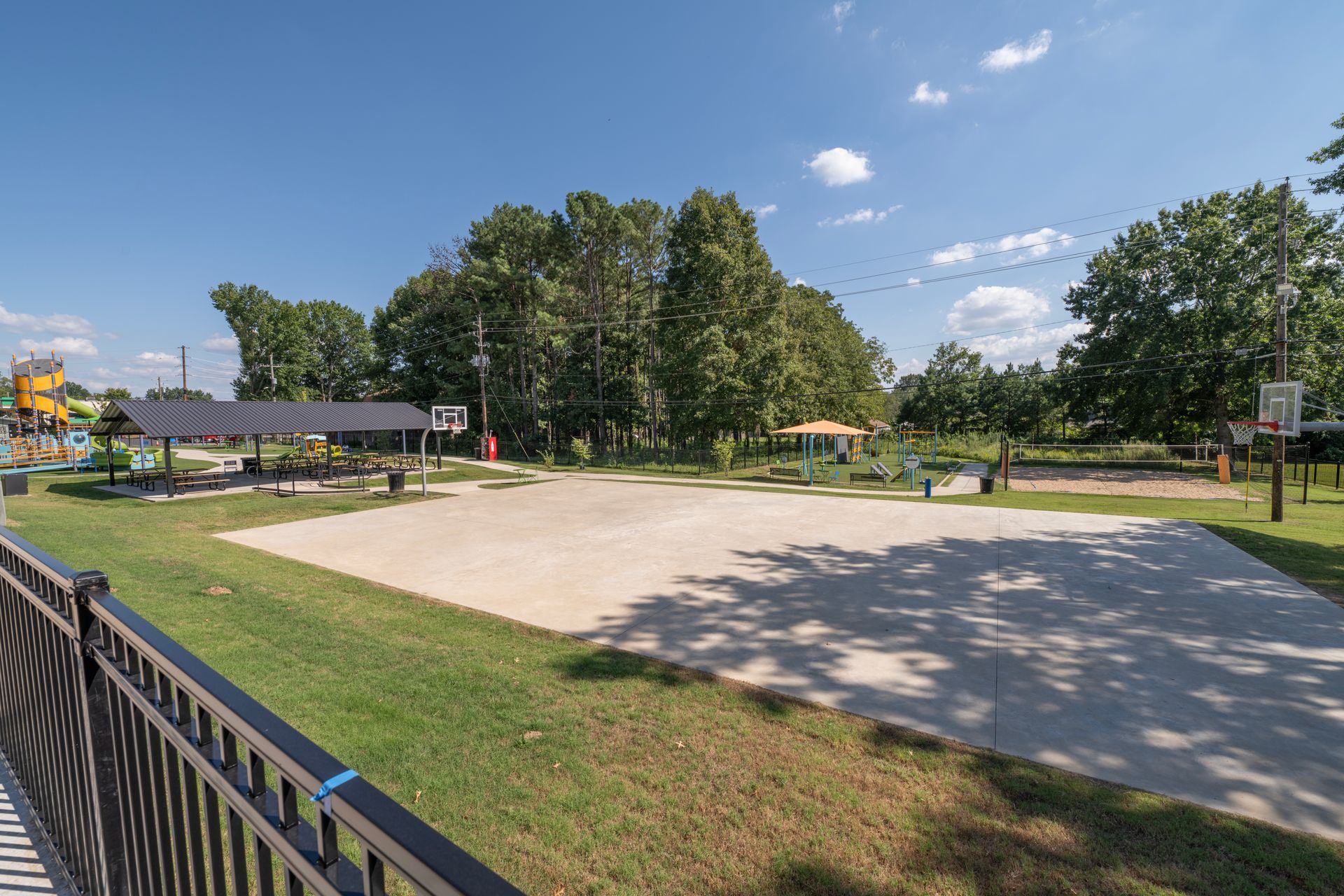 Sandy outdoor basketball court with a green grassy area and trees on a sunny day.