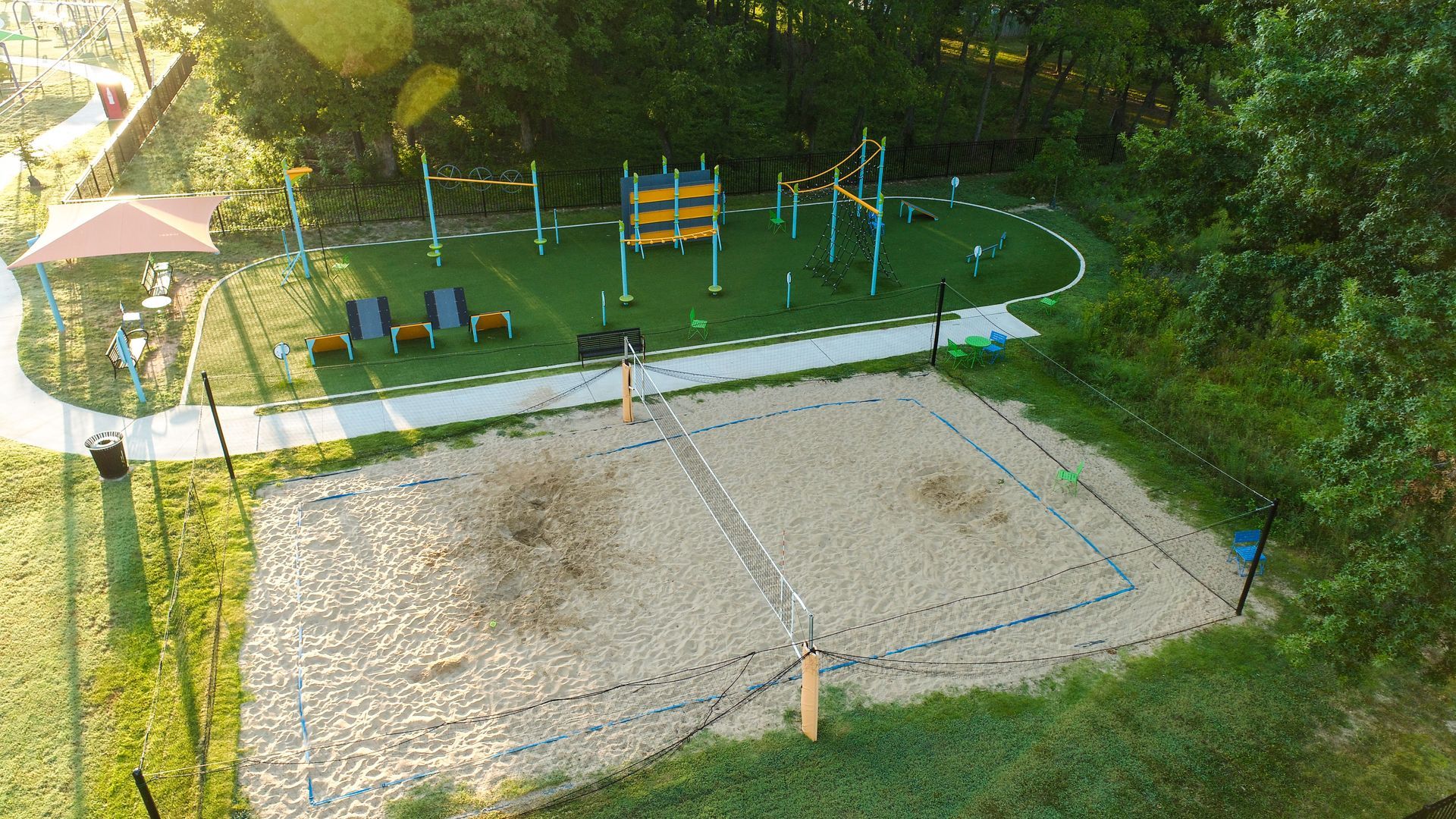 Aerial view of a sand volleyball court and outdoor fitness area in a park.