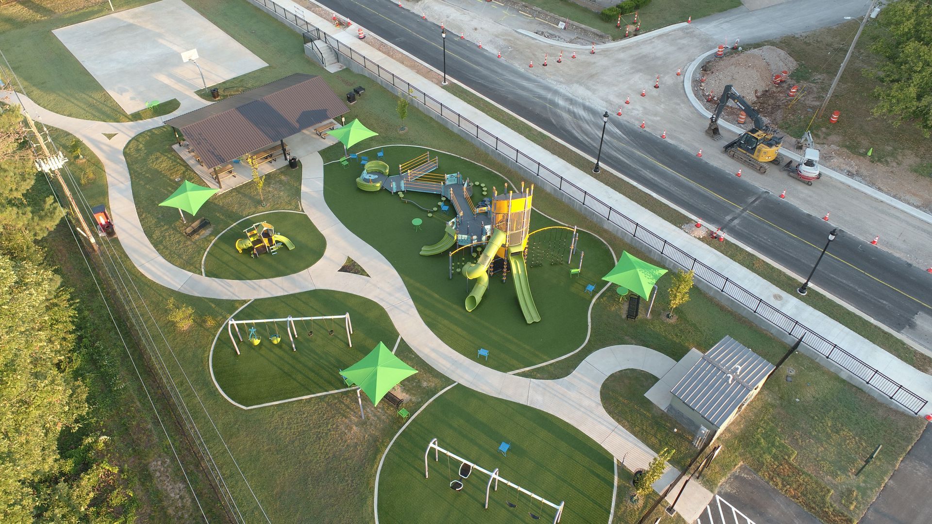 Aerial view of a playground with green structures, walkways, shade canopies, and a basketball court.