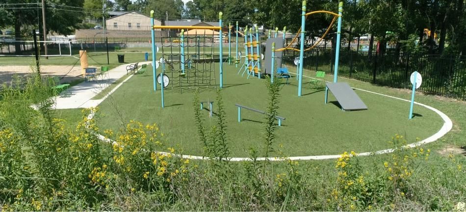 Playground with green turf, various climbing structures, and a concrete path.