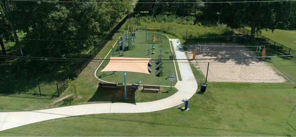A park with a playground, a sand pit, and a walking path surrounded by trees and grass.