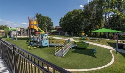 Playground with colorful equipment, green turf, and trees under a clear blue sky.