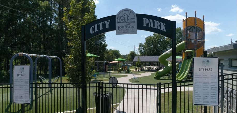 Entrance to City Park with archway sign, playground equipment, and information sign.
