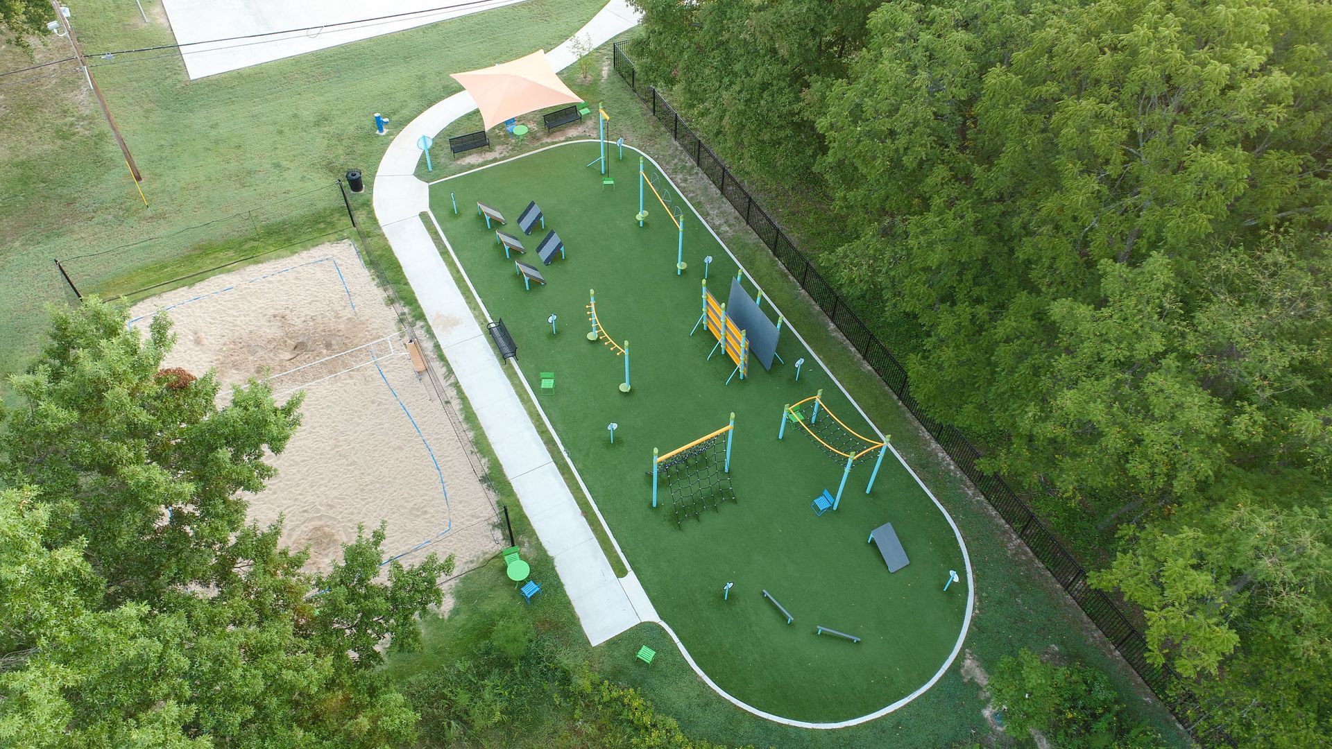 Aerial view of dog park with green turf, agility equipment, and a walking path.