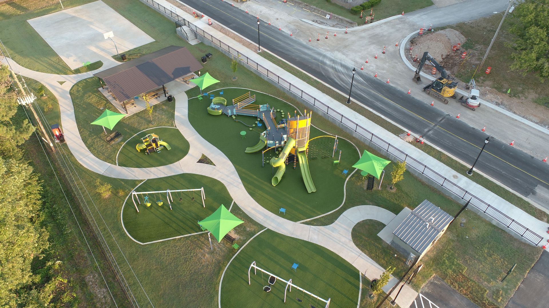 Aerial view of a playground with walking paths, swings, and climbing structures; green and brown color scheme.