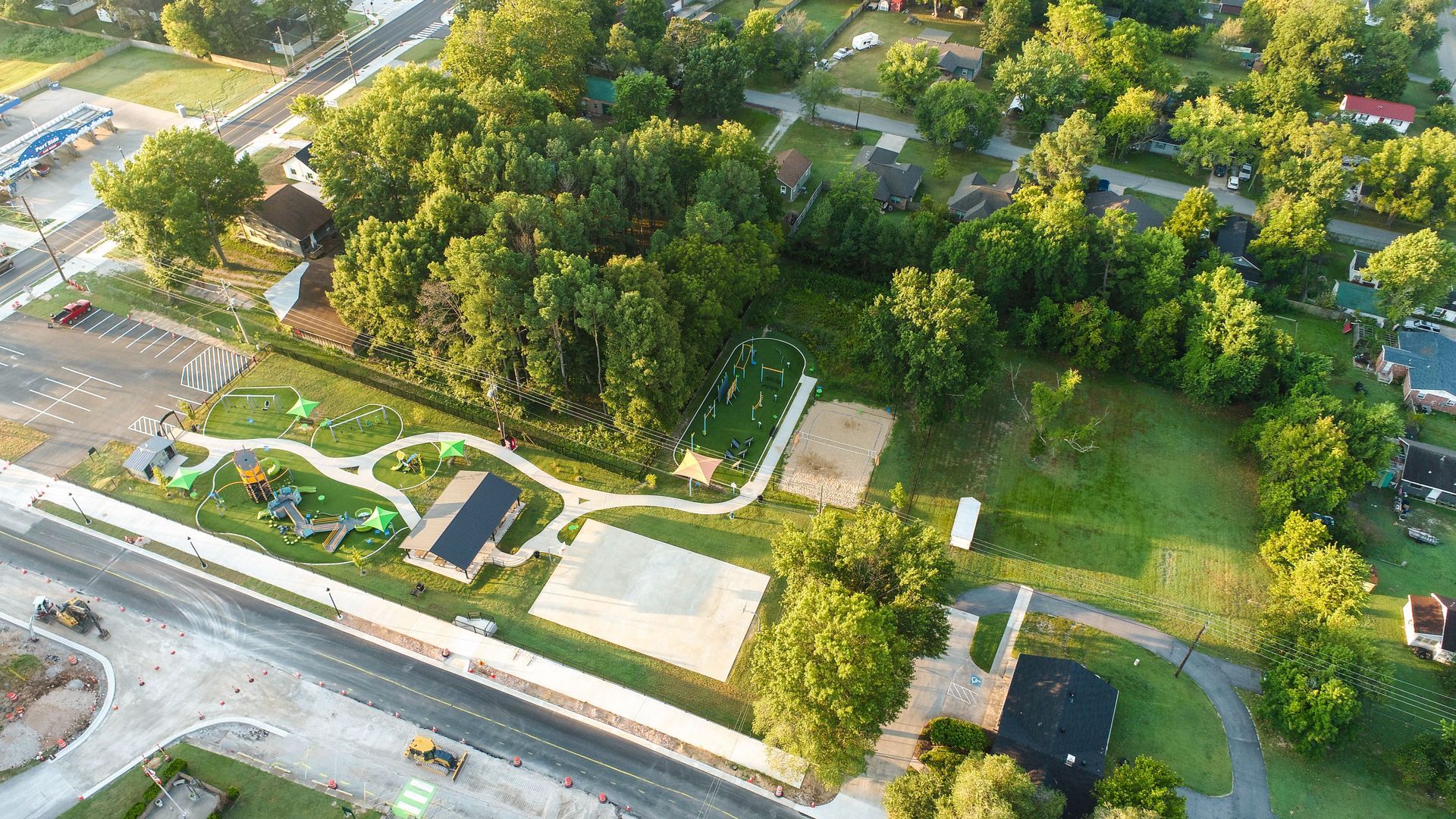 Aerial view of a park with playground, basketball court, and trees near a road and buildings.
