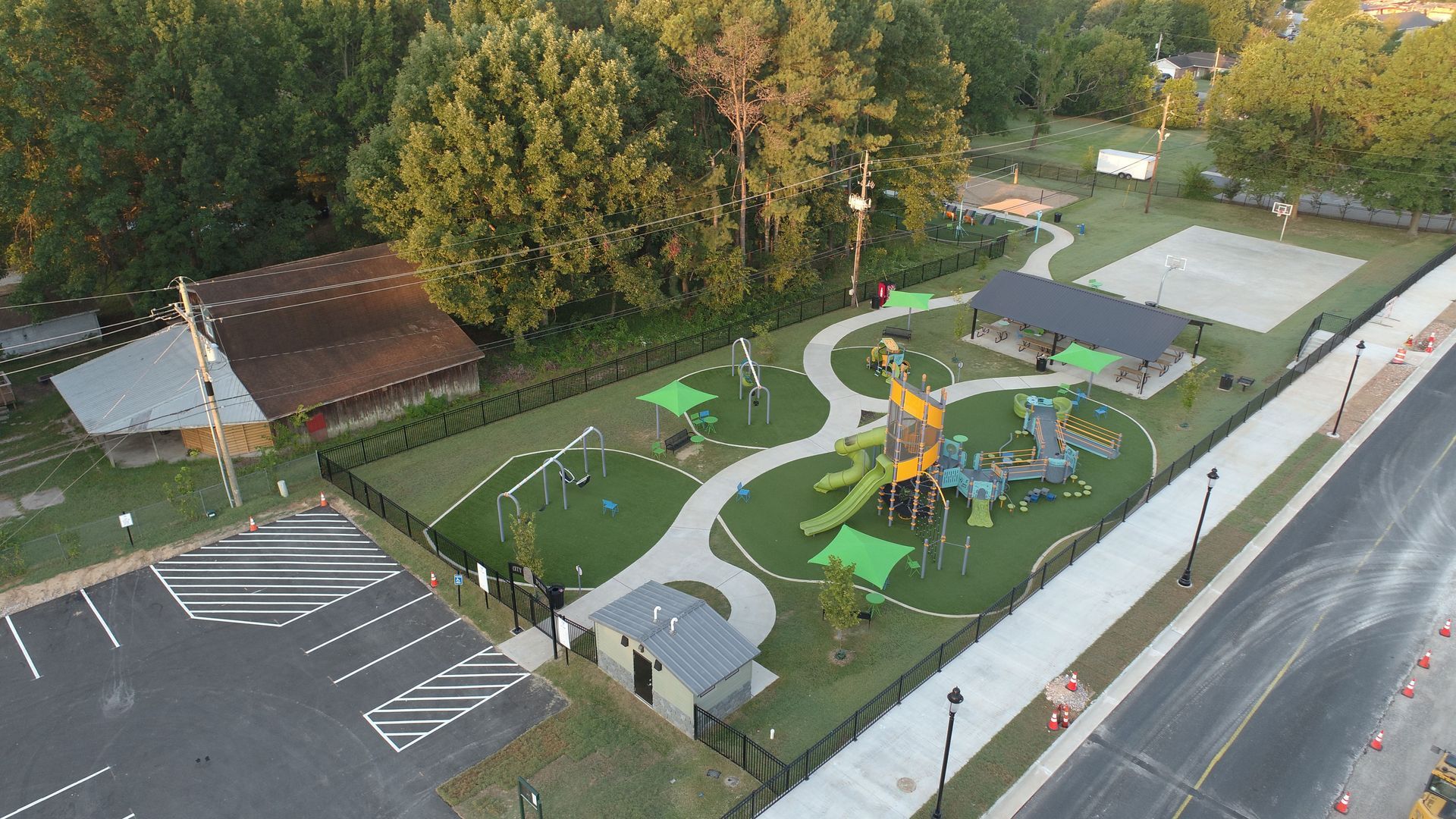 Aerial view of a playground with play structures, paths, and a covered shelter, surrounded by a fence.