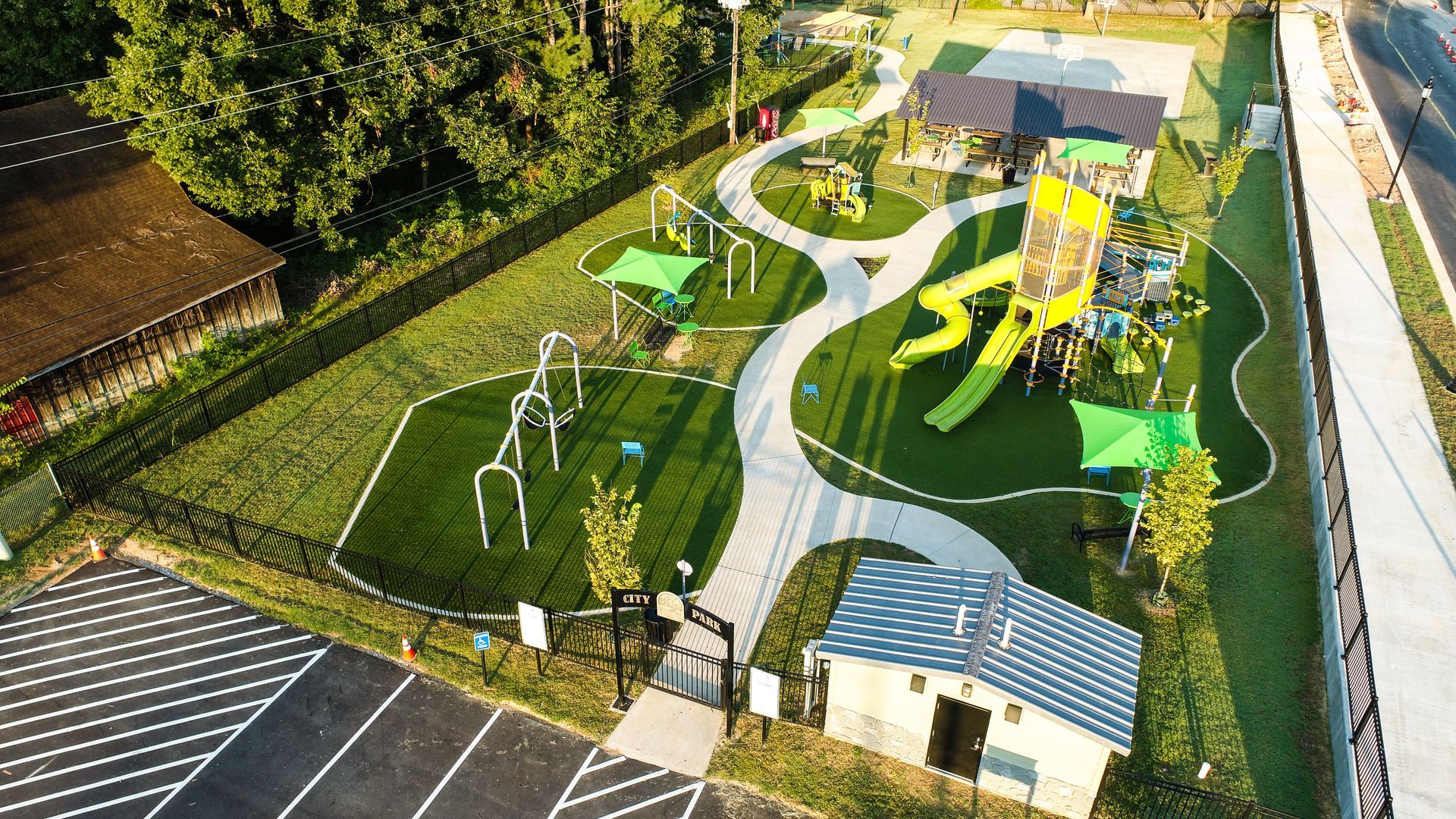 Aerial view of a playground with swings, slides, a winding path, and green turf.