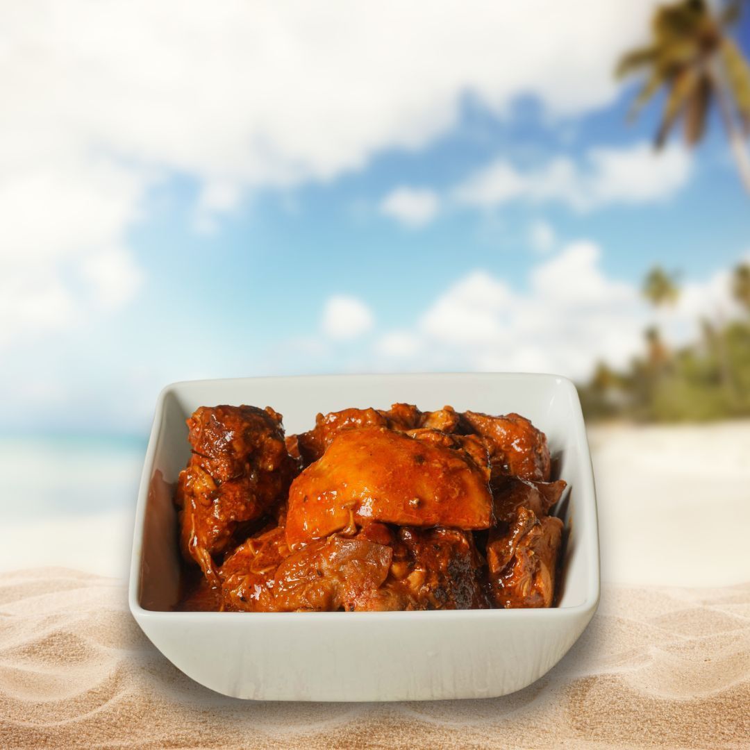 A white bowl of orange curry with cilantro and lime wedge on a sandy beach with a tropical background.