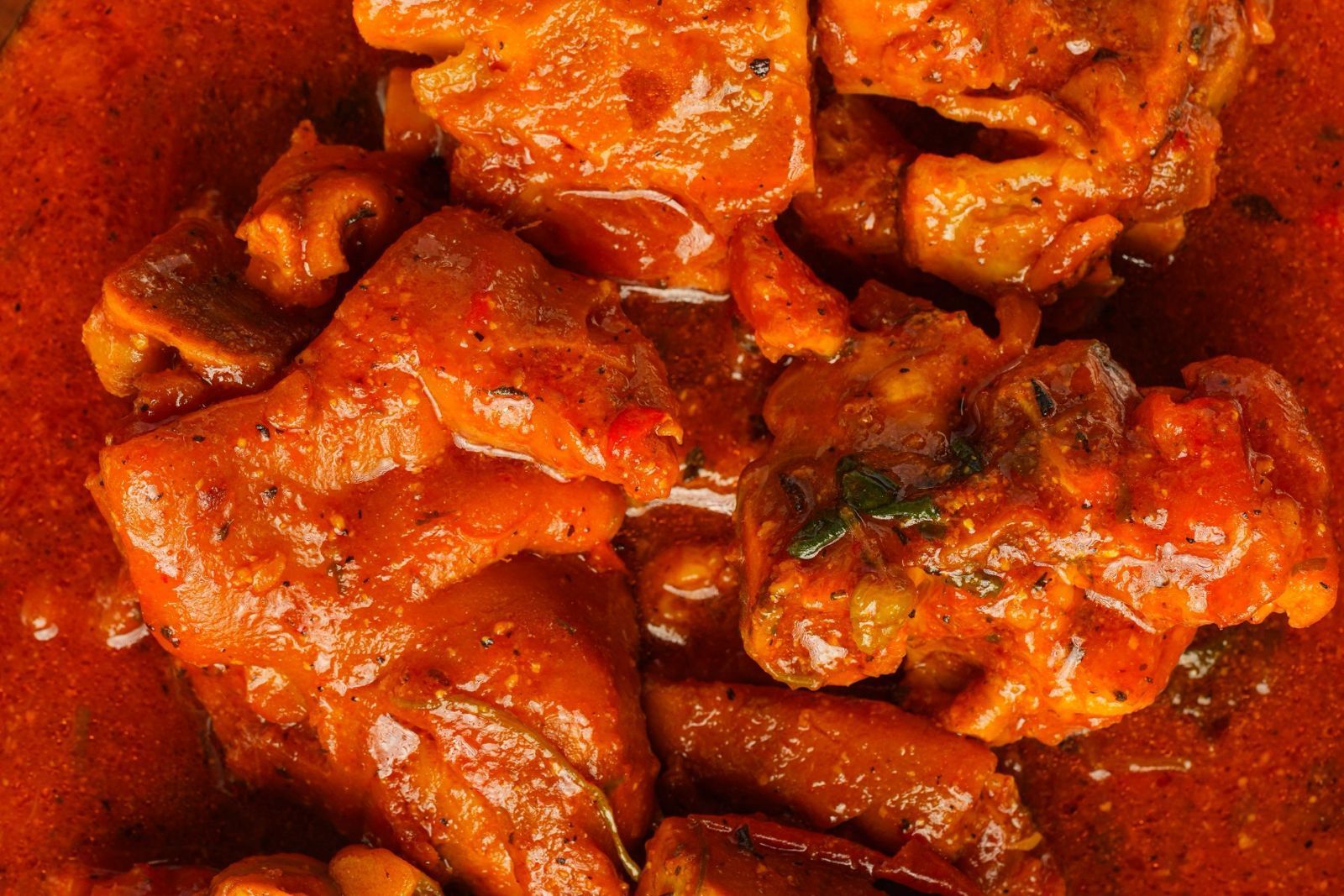 Close-up of a spicy, red stew with large chunks of meat. The stew appears oily and flavorful, possibly a curry.