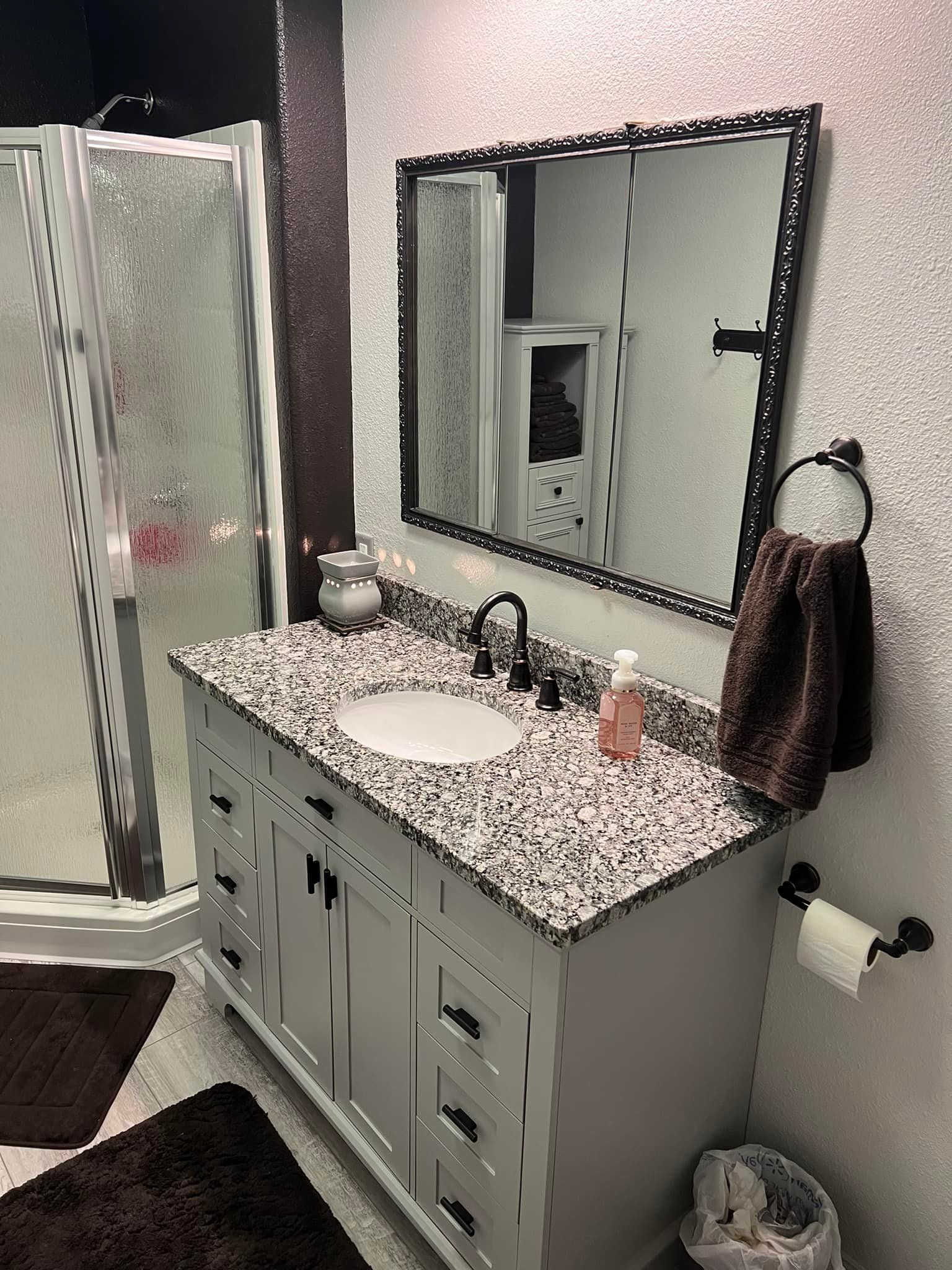 Bathroom with a white vanity, granite countertop, and shower stall. Brown accents and mirror.