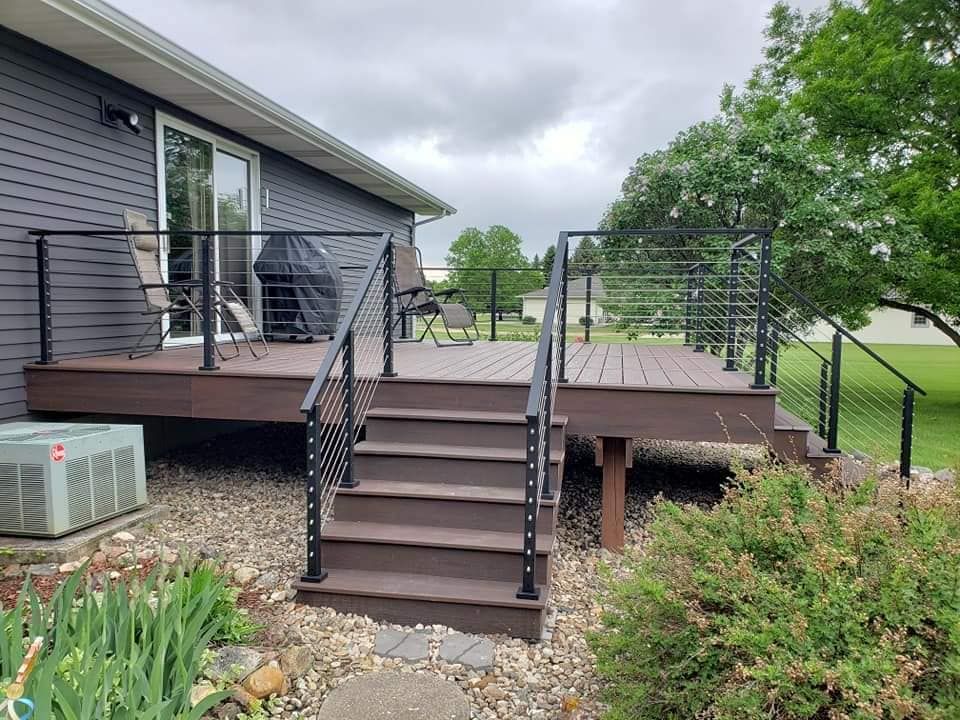 A multi-level deck with cable railings. Brown composite decking, black railings, and a gray house. Overcast sky.