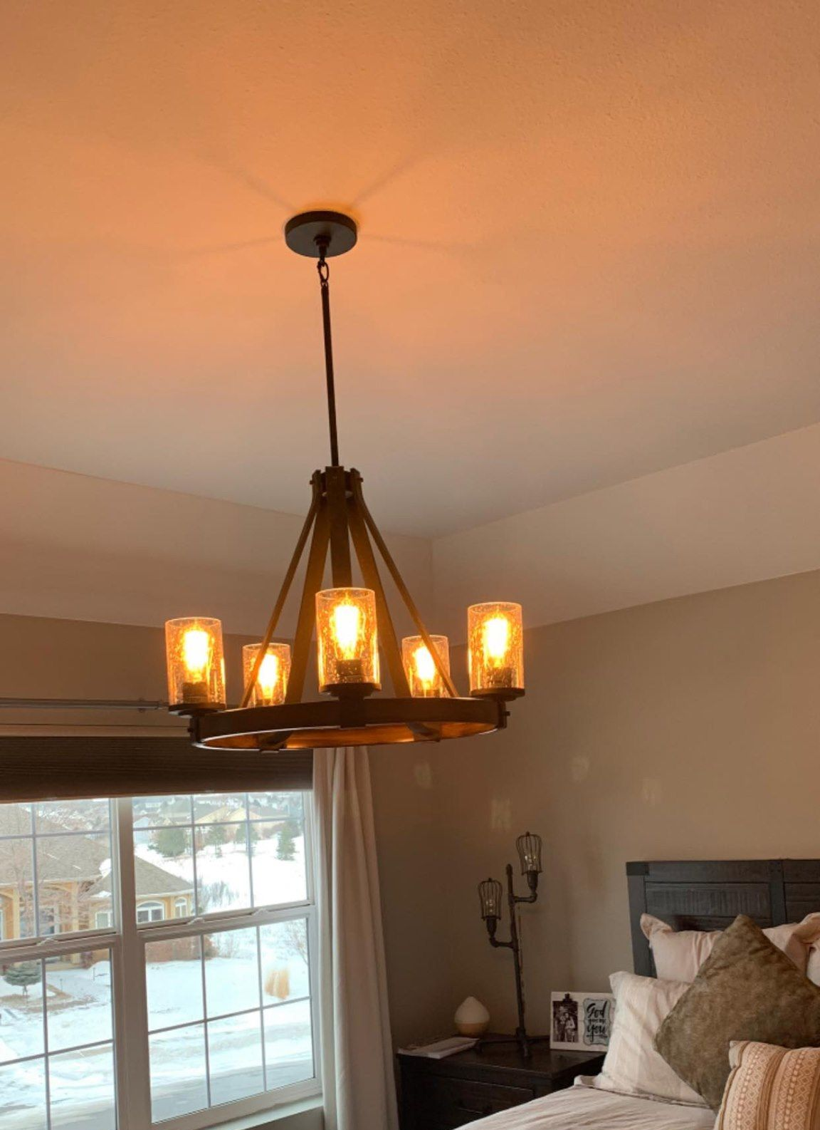 Chandelier hanging from ceiling, illuminating a bedroom. Features warm light and glass shades.