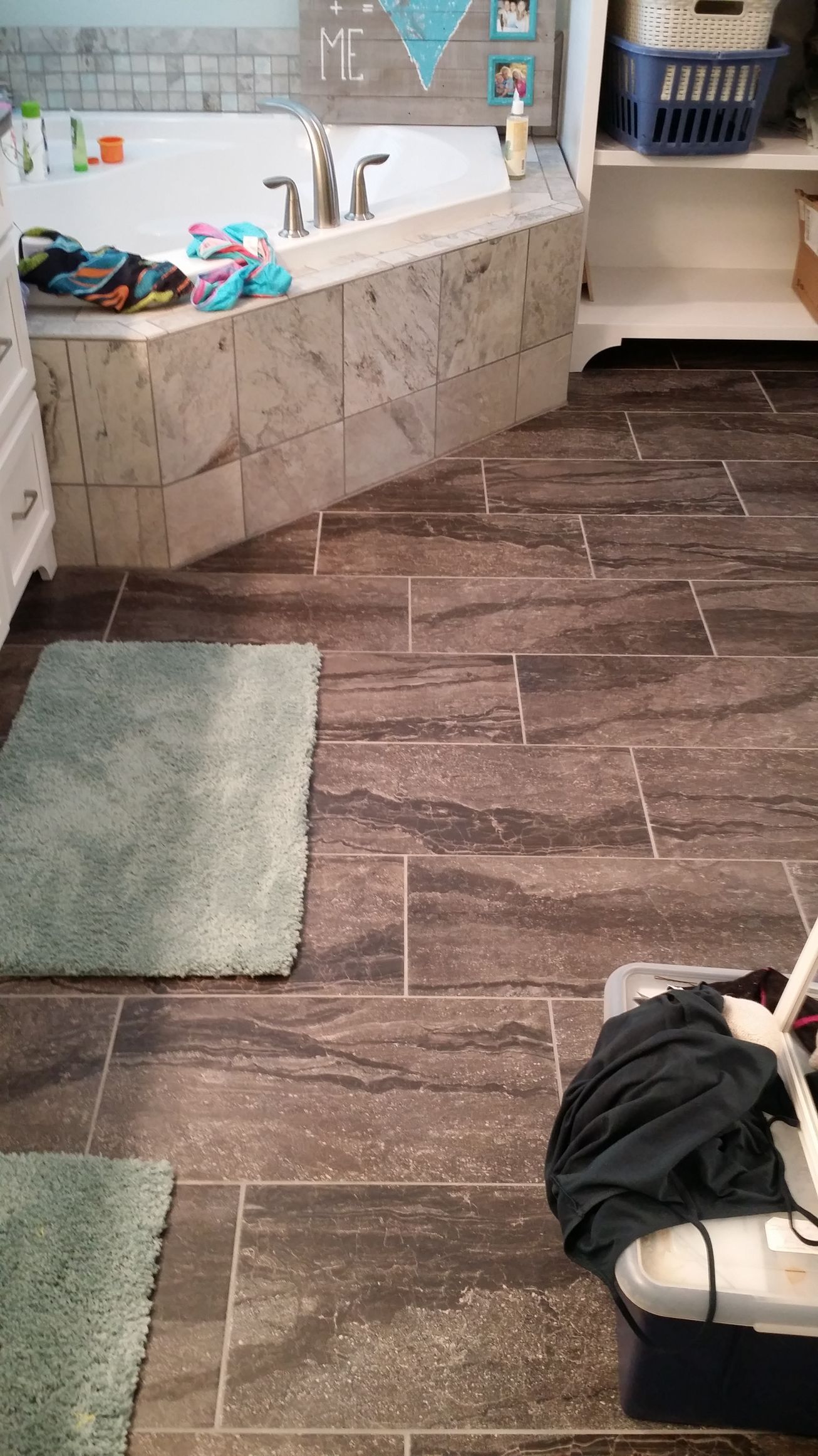 Bathroom with brown tiled floor, a built-in tub, and two teal bath mats.