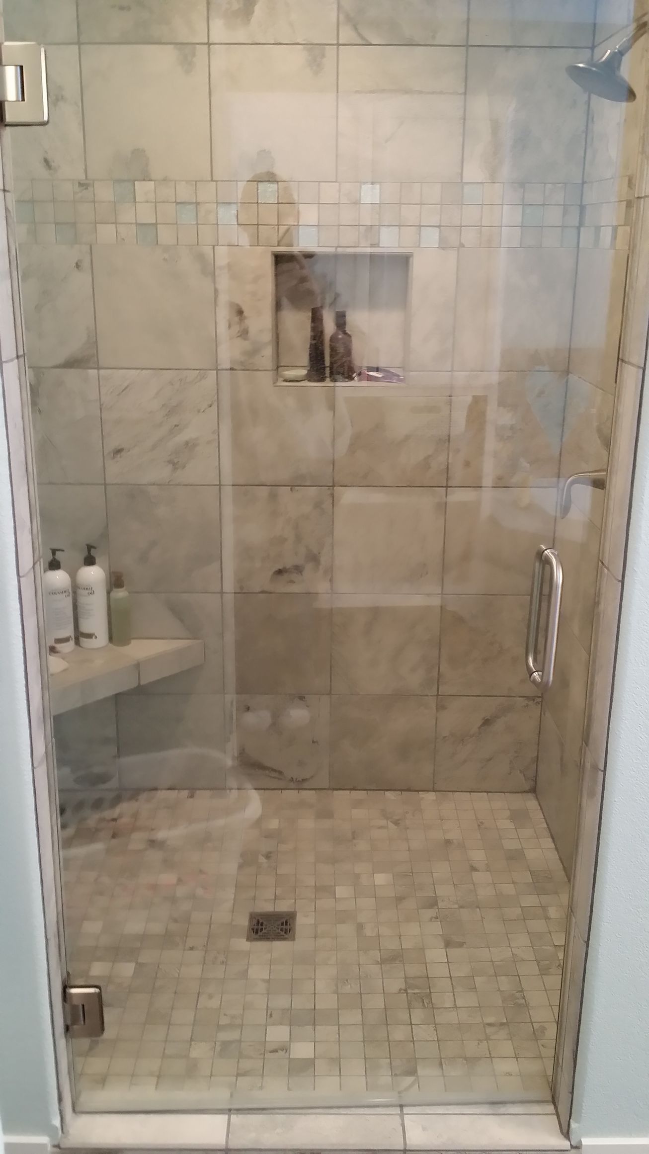 Glass shower with marble tile, built-in bench, and recessed shelf for toiletries.